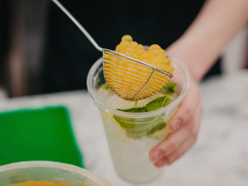 Pea ladle being used to pour yellow boba balls into a DIY bubble tea drink garnished with mint